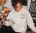 Model wearing cream hoodie with Hey There Pumpkin embroidery on left chest, sitting on a fall porch