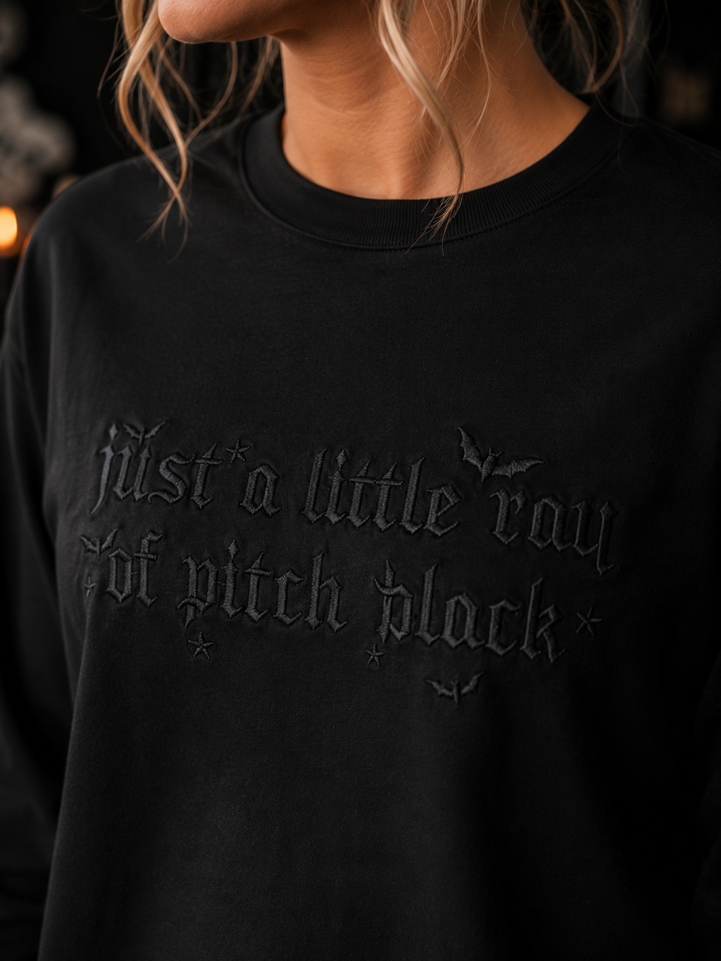 Woman wearing a black Gildan Ultra Cotton
long sleeve shirt featuring black embroidered
lettering reading "Just a Little Ray of Pitch Black"
with bat accents.