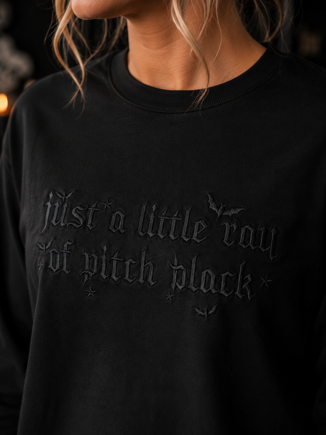 Woman wearing a black Gildan Ultra Cotton
long sleeve shirt featuring black embroidered
lettering reading "Just a Little Ray of Pitch Black"
with bat accents.